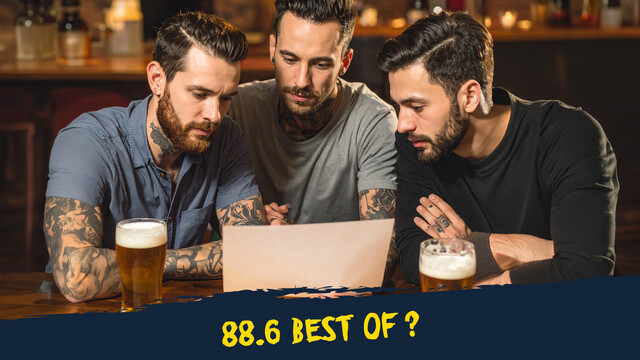 drei tätowierte Männer sitzen an einem Tisch in einem Pub, trinken Bier und schauen auf einen Zettel