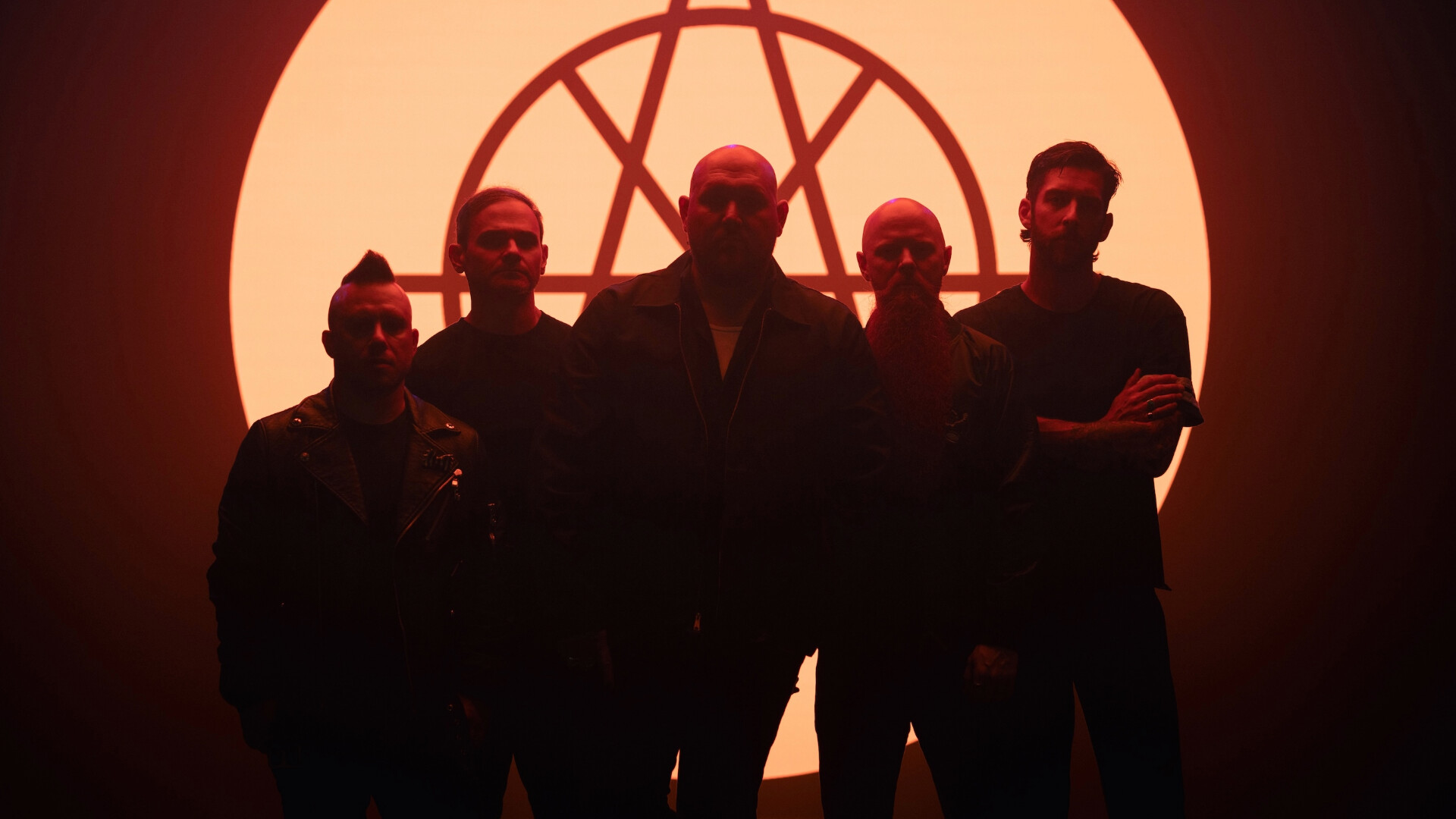 Die Bandmitglieder von Atreyu stehen in einem dunklen Raum vor einem leuchtenden Logo