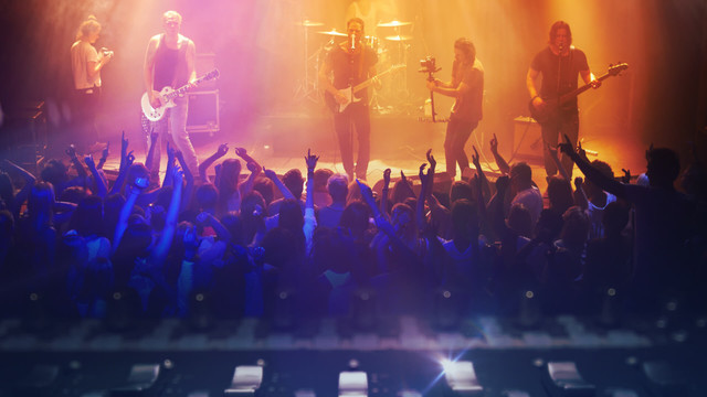 Eine Rockband steht vor einem jubelnden Publikum auf der Bühne