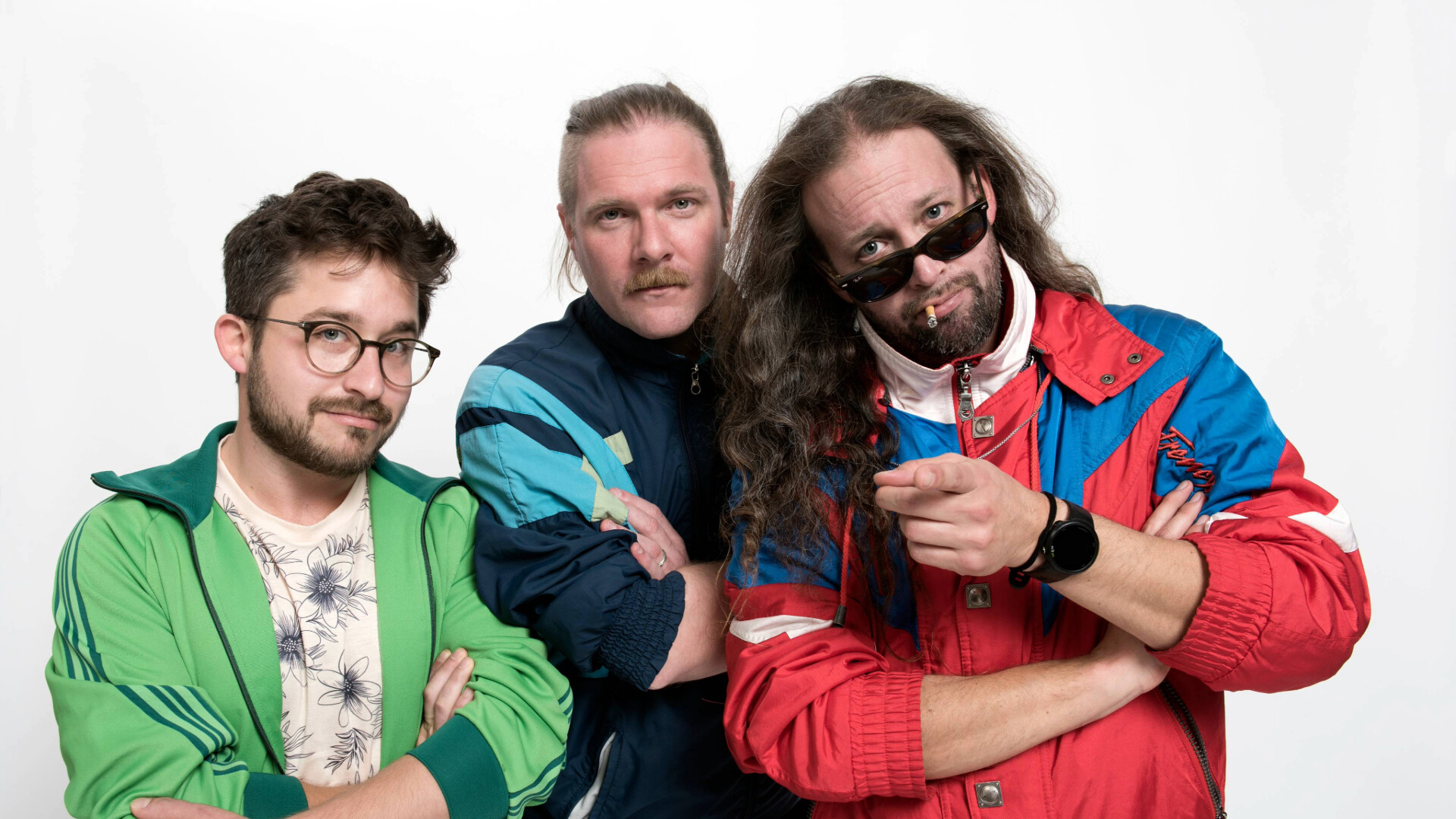 Die Band steht in Retro Trainingsanzügen vor neutralem Hintergrund