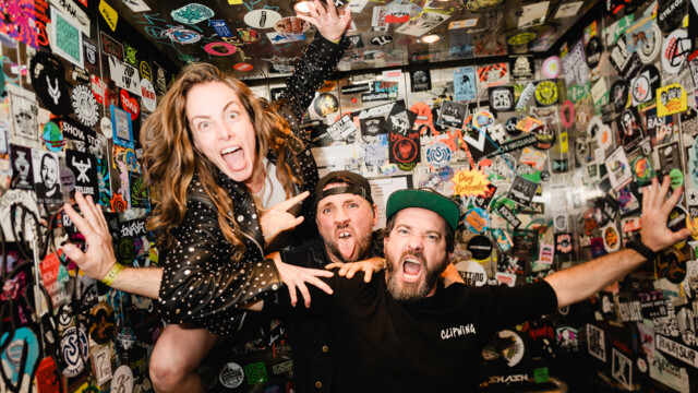 Die Band posiert in einem engen Raum voller Sticker