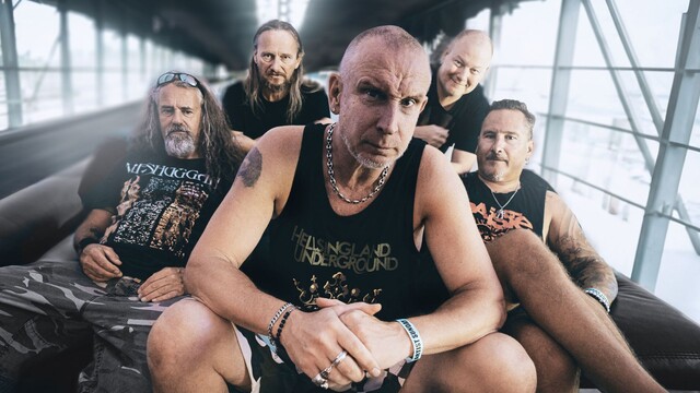 Die Bandmitglieder von Clawfinger sitzen auf einer Couch in einem Langen Gang mit Fenstern auf den Seiten