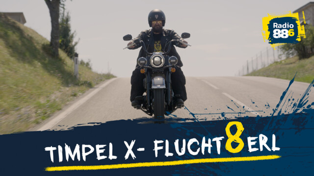Timpel sitzt auf einem Motorrad und fährt auf einer Freilandstraße, links und rechts sind Wiese und Bäume
