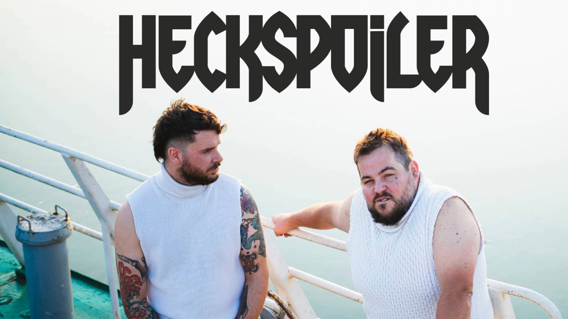 Das Heckspoiler Duo steht in weißen Rollkragenpullis auf einem Schiff