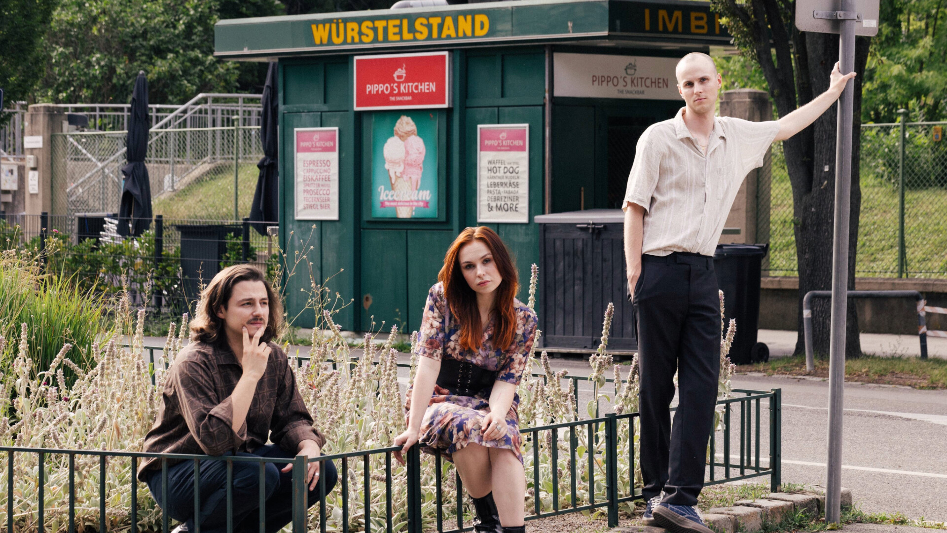 Die Band posiert in einer kleinen Wiese vor einem Würstelstand