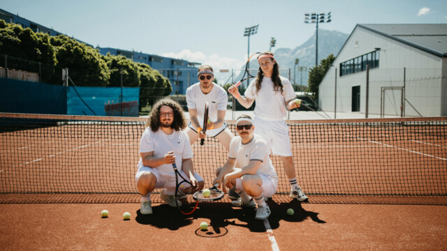 Die Band posiert in weißen Retro Tennisoutfits auf einem Tennisplatz mit den Bergen im Hintergrund