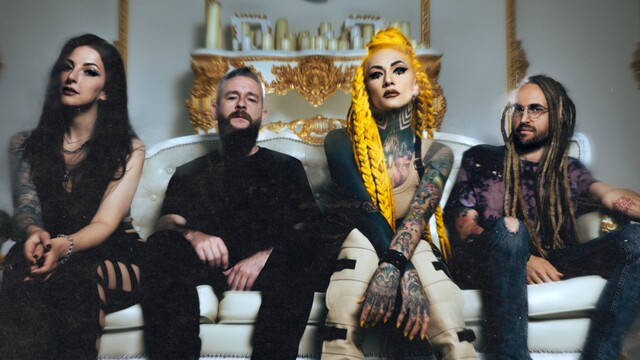 Die Band sitzt auf einem Weißen Sofa, der Hintergrund ist mit Gold verziert