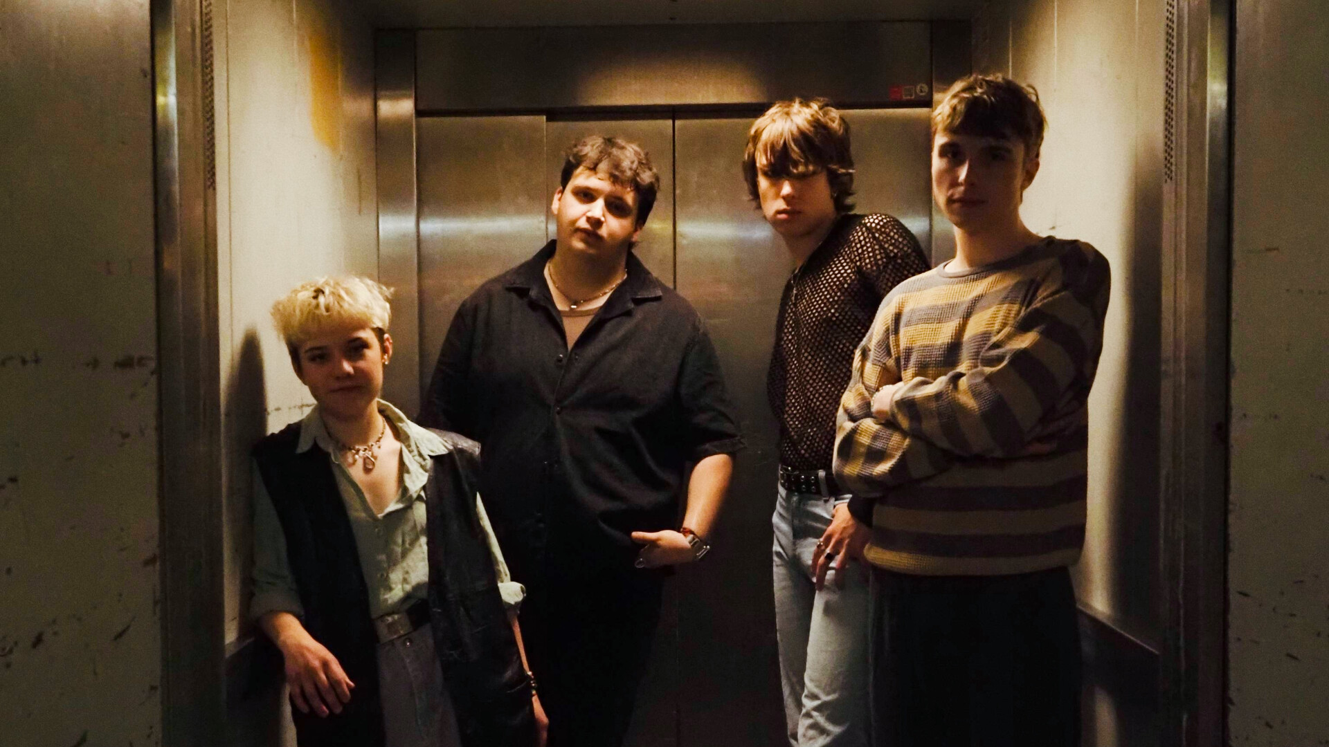 Die Band posiert zu viert in einem Aufzug