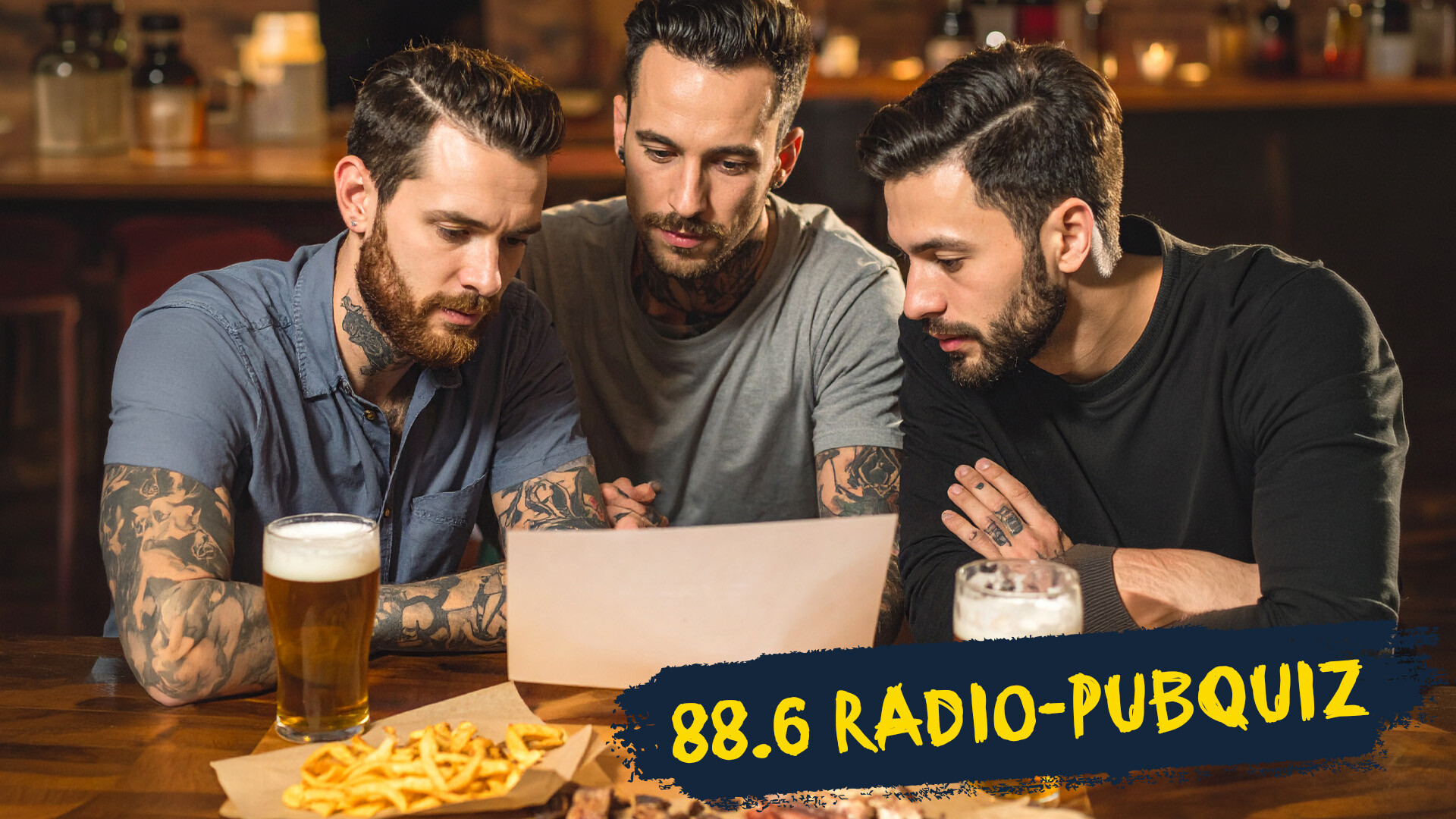 drei tätowierte Männer sitzen an einem Tisch in einem Pub, trinken Bier und schauen auf einen Zettel